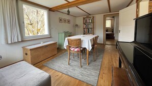Um quarto aconchegante com piso de madeira, uma mesa de jantar com cadeiras, um sofá, uma televisão e uma estante de livros.