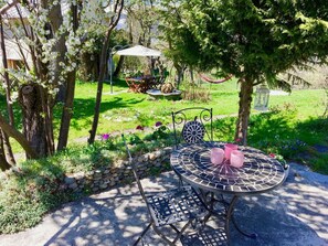 A patio with a round table and chairs, surrounded by greenery and a stone wall.