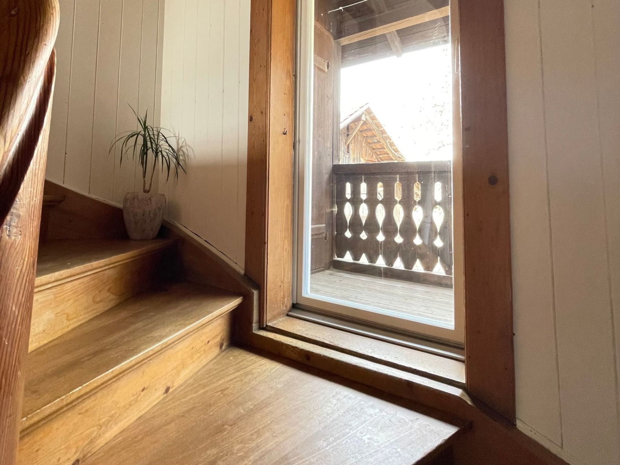 Una escalera de madera que lleva a un balcón con vista a una terraza de madera y una valla.