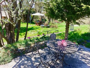 An outdoor patio with a round table and chairs, surrounded by greenery and a stone wall. - Ferienhaus Casa Marili Schmed, Sevgein, (Sevgein), 27001B by Interhome (Sevgein)