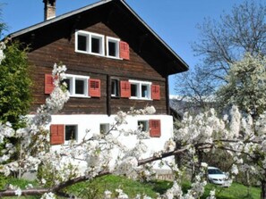 A two-story building with a sloped roof, multiple windows with shutters, and a car parked in front. - Ferienhaus Casa Marili Schmed, Sevgein, (Sevgein), 27001B by Interhome (Sevgein)