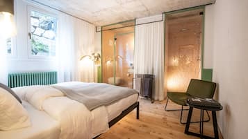 Een slaapkamer met een bed, een stoel, een radiator, een raam en een douchegedeelte.