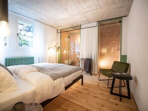 A bedroom with a bed, a chair, a radiator, a window, and a shower area. - Tremondi Boutique BNB & Restaurant, (Quinten), by Interhome (Quinten)