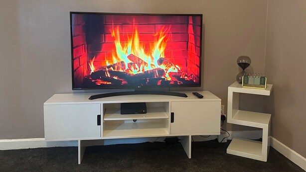 Televisor de pantalla plana muntat sobre un moble blanc amb un comandament a distància i una petita estant amb un calendari.