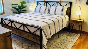 A bedroom with a bed, a ceiling fan, a nightstand, a lamp, a plant, and artwork on the walls. - Charming 3-bedroom cabin with White River views! (Melbourne)