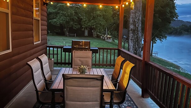 A wooden deck with a table and chairs, a grill, and a view of a lake. - Charming 3-bedroom cabin with White River views! (Melbourne)