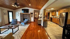 A spacious living area with a fireplace, wooden flooring, and a television mounted above it. - Charming 3-bedroom cabin with White River views! (Melbourne)