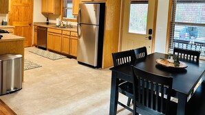 A modern kitchen with wooden cabinets, stainless steel appliances, and a dining area with a table and chairs. - Charming 3-bedroom cabin with White River views! (Melbourne)