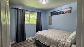 A bedroom with a bed, a window with curtains, a nightlight, and a cityscape painting on the wall. - Updated Modern Country Home - Pristine & Quiet - Near Seattle & Tacoma (Kent)