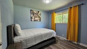 A single bed in a room with light blue walls, a window with yellow curtains, and a wall-mounted picture.