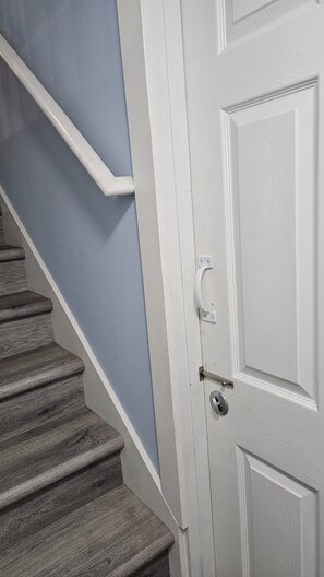 Une porte blanche avec une poignée argentée et un trou de serrure, située à côté d’un escalier en bois avec des marches et une rampe blanche.