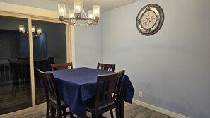 A dining area with a table set for four, a chandelier, and a wall clock.