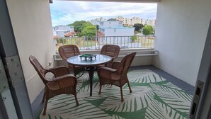 Un balcon avec une table et des chaises, un tapis à motifs et une vue sur des immeubles et des arbres.