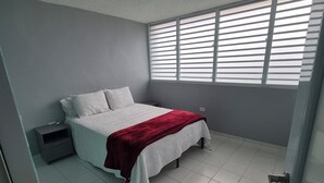 Une chambre à coucher avec un lit, une table de chevet et des stores aux fenêtres.