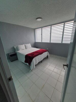 A bedroom with a bed, nightstand, and window blinds. - Coastal Retreat at Villa Marina The Village,  Beaches ,Boats & Sea adventures!!! (Fajardo)