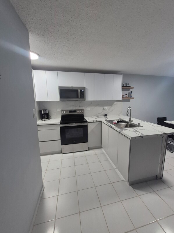 A modern kitchen with white cabinets, a microwave, an oven, and a sink. - Coastal Retreat at Villa Marina The Village,  Beaches ,Boats & Sea adventures!!! (Fajardo)