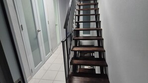 Un escalier avec des marches en bois et une rampe en métal, menant à une pièce dotée d’une porte blanche et de panneaux de verre dépoli.