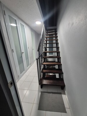 A staircase with wooden steps and a metal railing, leading to a room with a white door and frosted glass panels. - Coastal Retreat at Villa Marina The Village,  Beaches ,Boats & Sea adventures!!! (Fajardo)