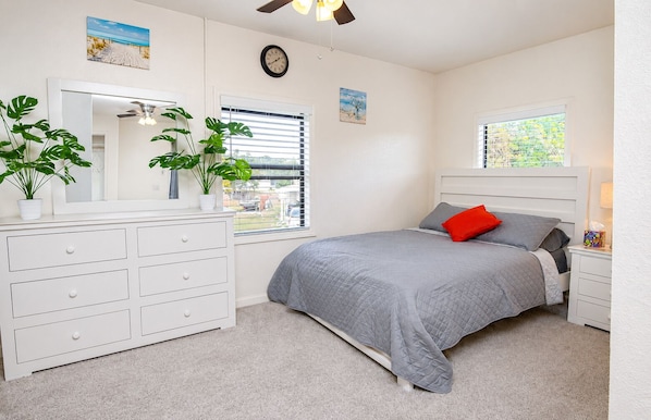 A bedroom with a bed, dresser, two windows, a ceiling fan, and a clock.