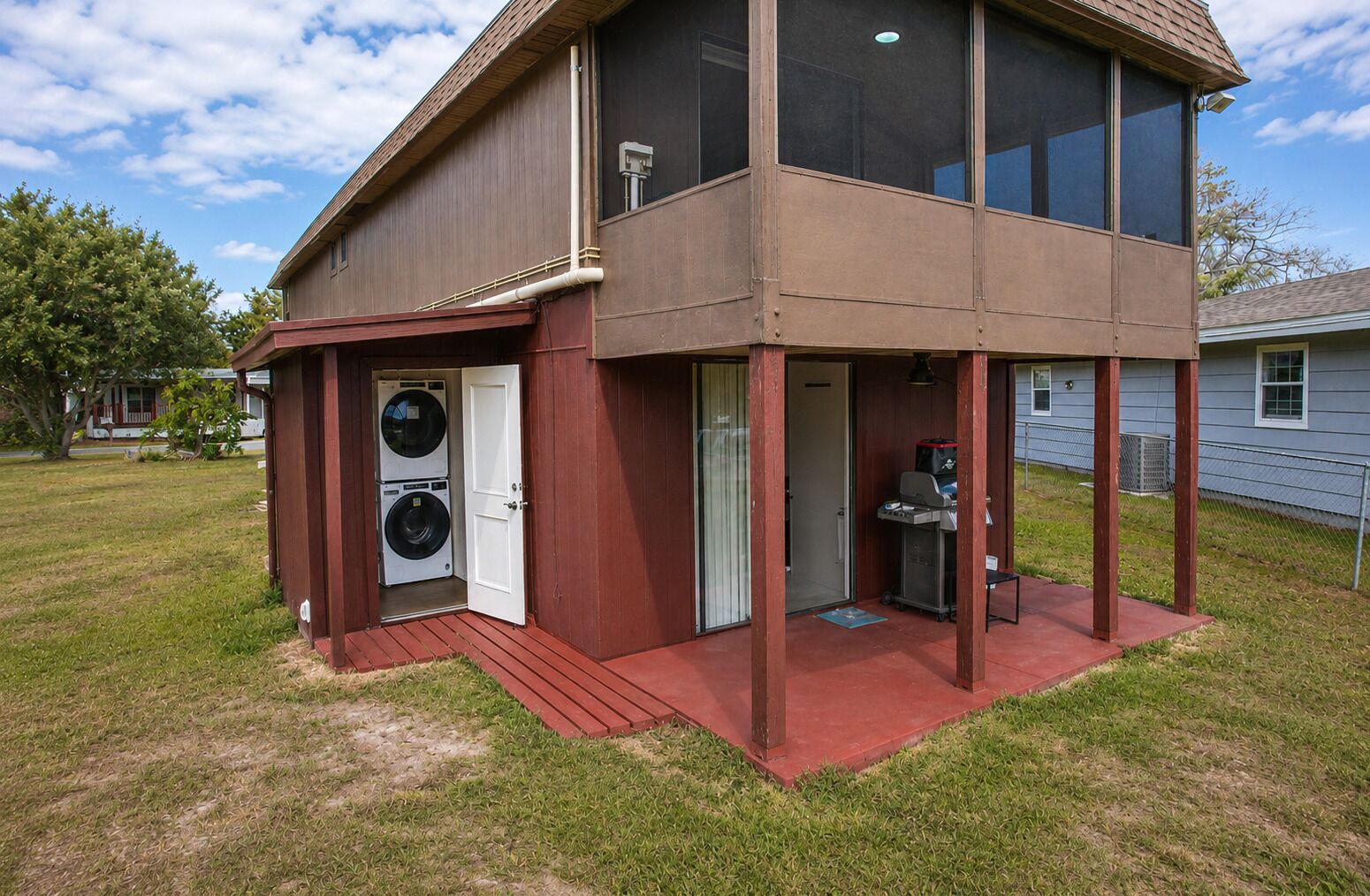 A two-story building with a laundry room on the ground floor and a covered outdoor area with a grill.