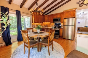 A modern kitchen with wooden cabinets, stainless steel appliances, and a dining area with a round table and chairs. - Charming 3-bedroom house in Arrowhead Lake (Pocono Lake)