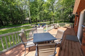 A wooden deck with outdoor furniture, a table, and chairs. - Charming 3-bedroom house in Arrowhead Lake (Pocono Lake)