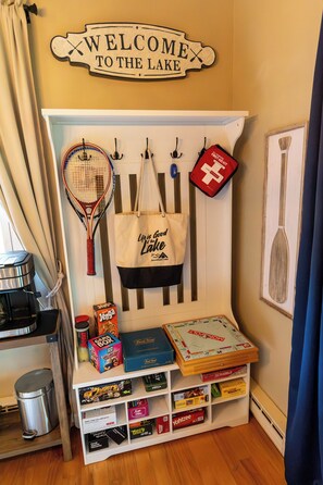 A room with a welcome sign, a rack with a bag, and a shelf with board games. - Charming 3-bedroom house in Arrowhead Lake (Pocono Lake)