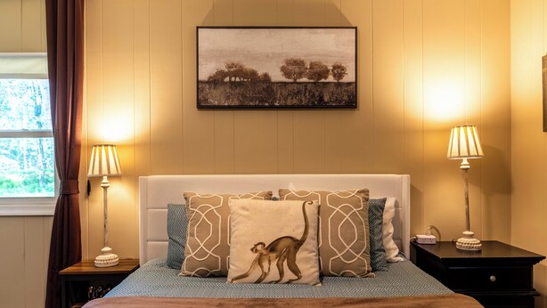 Een slaapkamer met een bed, twee nachtkastjes met lampen, een raam met gordijnen en een schilderij aan de muur.