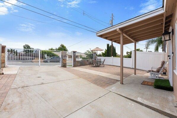 Un patio couvert avec une table et des chaises, une clôture blanche et une entrée fermée par un portail.
