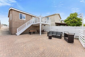 Un patio con mobiliario exterior, una escalera blanca y un edificio de fachada color beige.