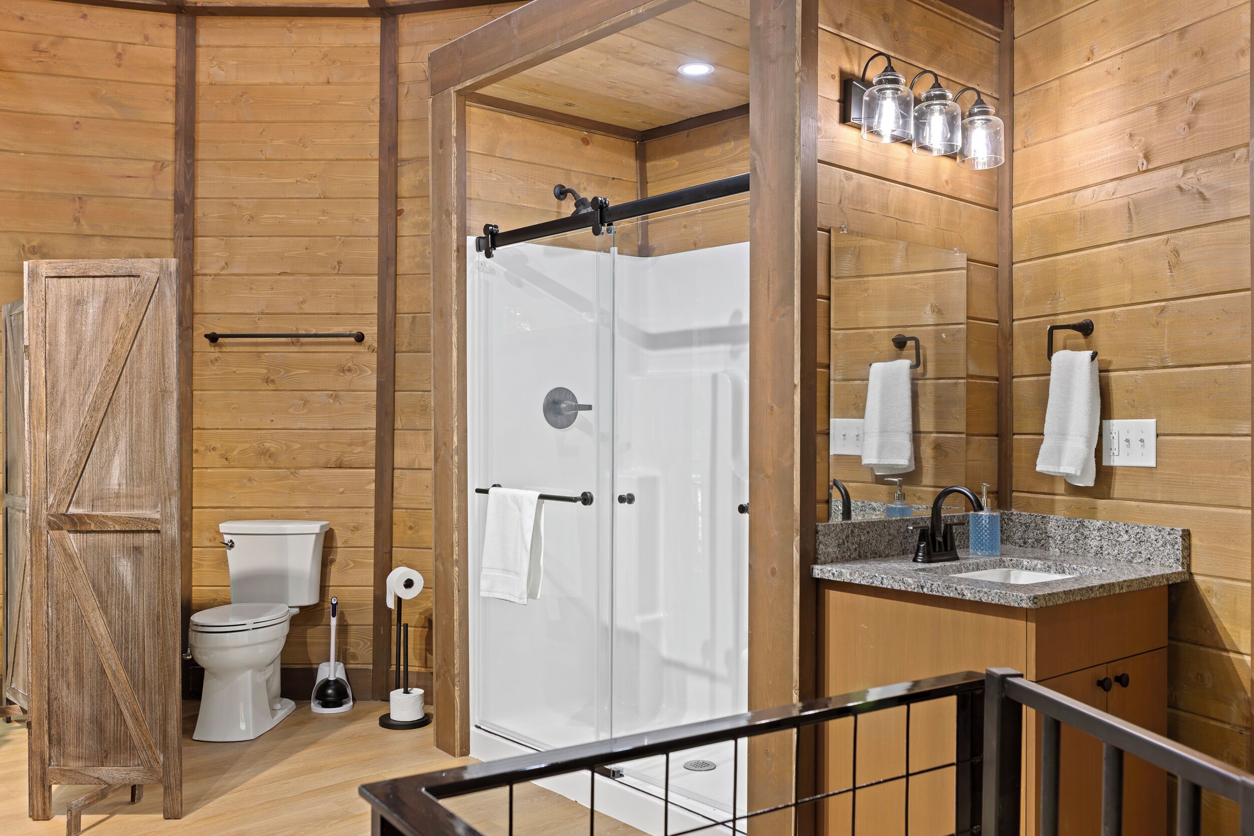 Un interior de madera con un inodoro blanco, cabina de ducha y lavabo con espejo.