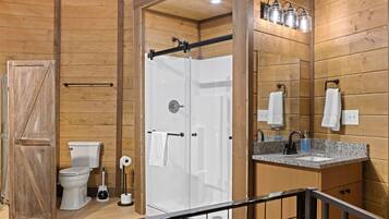 Un interior de madera con un inodoro blanco, cabina de ducha y lavabo con espejo.
