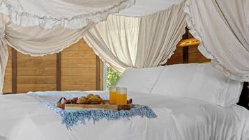 A bed with a canopy, a tray with muffins and a glass of juice, and a blue knitted throw.