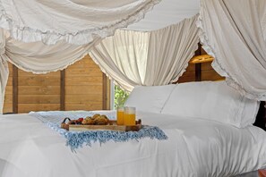 A bed with a canopy, a tray with muffins and a glass of juice, and a blue knitted throw.
