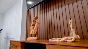 Un escritorio de madera con una escultura de madera, un florero con ramas de juncos y un rosario.