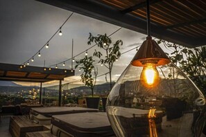 Un espacio al aire libre con luces colgantes, vistas despejadas de la ciudad y un gran parasol de vidrio.