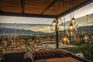 Interior de un edificio alto con un sofá de cuero, lámparas colgantes de vidrio y vistas a la ciudad.