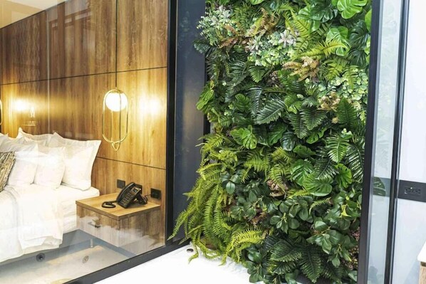 Una camera d'albergo moderna con una parete in legno, un letto con biancheria bianca, un comodino con un telefono e un ampio giardino verticale.