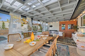 Un área de comedor al aire libre con una mesa de madera, sillas y una variedad de frutas y bebidas.