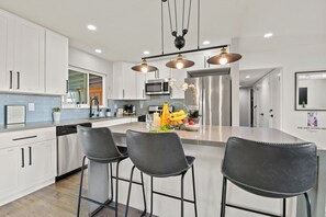 Una cocina moderna con gabinetes blancos, electrodomésticos de acero inoxidable y una isla central con taburetes de bar.
