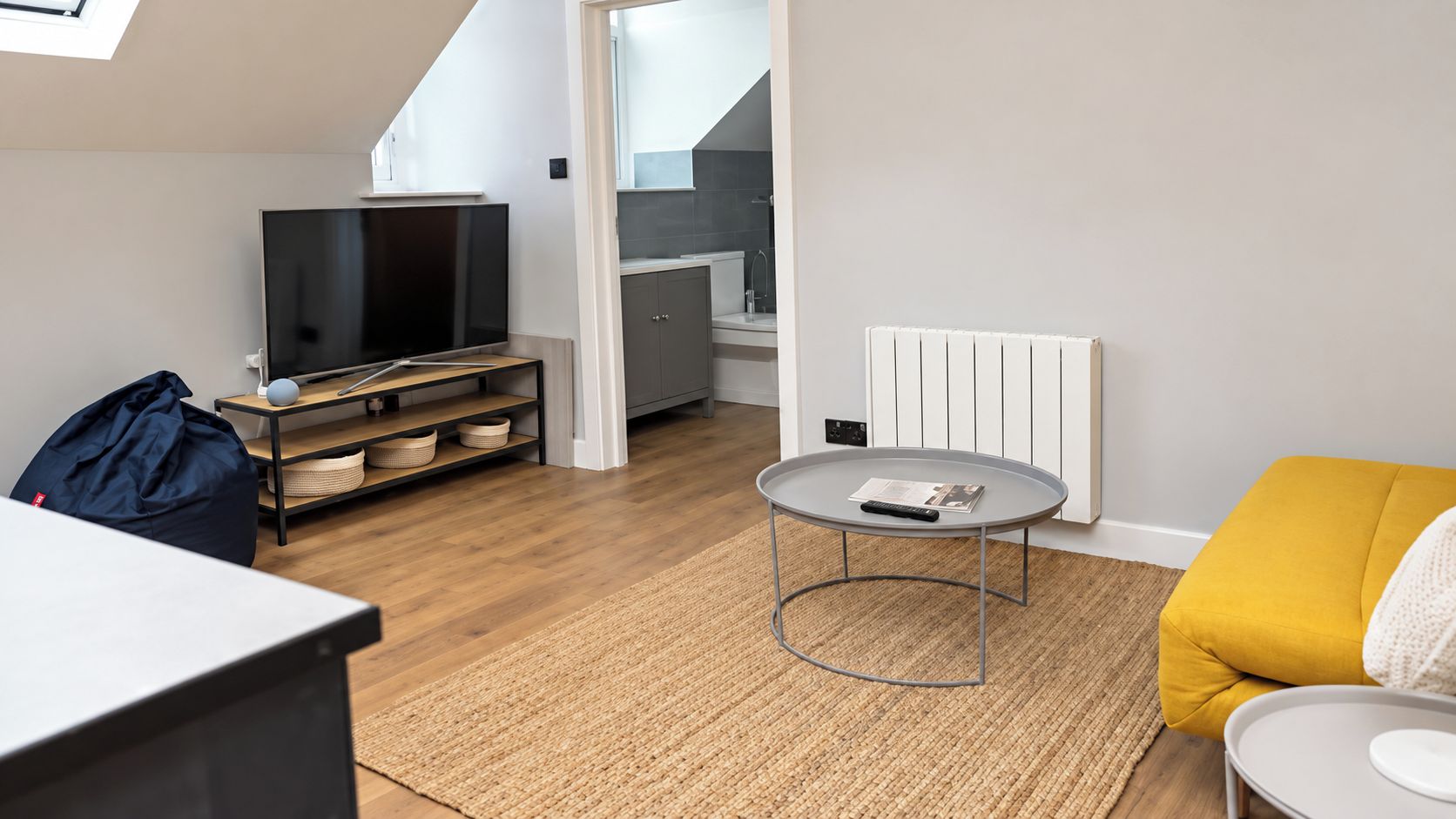 A modern living room with a flat-screen TV, a round coffee table, a sofa, and a kitchen area in the background.