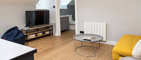 Una sala de estar moderna con un televisor de pantalla plana, una mesa redonda, un sofá y una cocina al fondo.