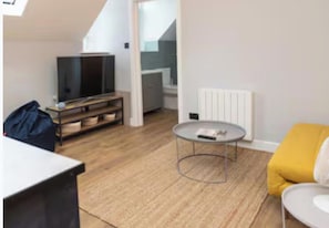 Ein modernes Wohnzimmer mit Fernseher, rundem Couchtisch und gelber Couch.