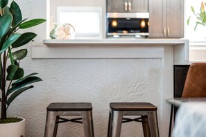 A kitchen with a white countertop, two stools, and a potted plant. - Casa Serena · Historic Spanish Home · SoSo (West Palm Beach)