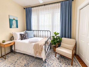 Une chambre à coucher avec un lit, une chaise, une table de chevet, une plante en pot et un tableau accroché au mur.
