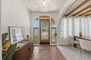Een gang met een houten bankje, een deur met ruitpanelen en een betegelde vloer.