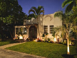 A house with a well-maintained lawn, a front porch, and a large window overlooking the yard. - Casa Serena · Historic Spanish Home · SoSo (West Palm Beach)