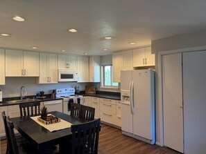 A modern kitchen with white cabinets, a microwave, stove, refrigerator, and a dining area with a table and chairs. - Perfect 3-bedroom condo in lovely Winter Park (Winter Park)