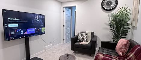 A modern living room with a flat-screen TV, a black leather sofa, a coffee table, and a potted plant.