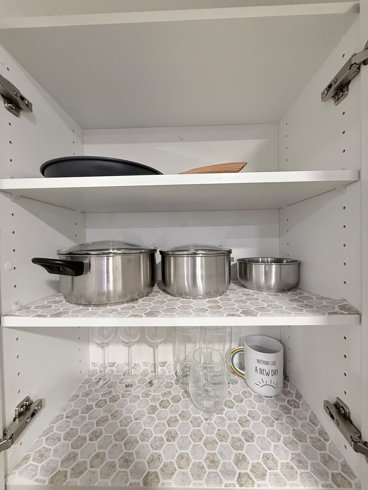 A kitchen with three stainless steel pots on the upper shelf and a white mug with text on the lower shelf.